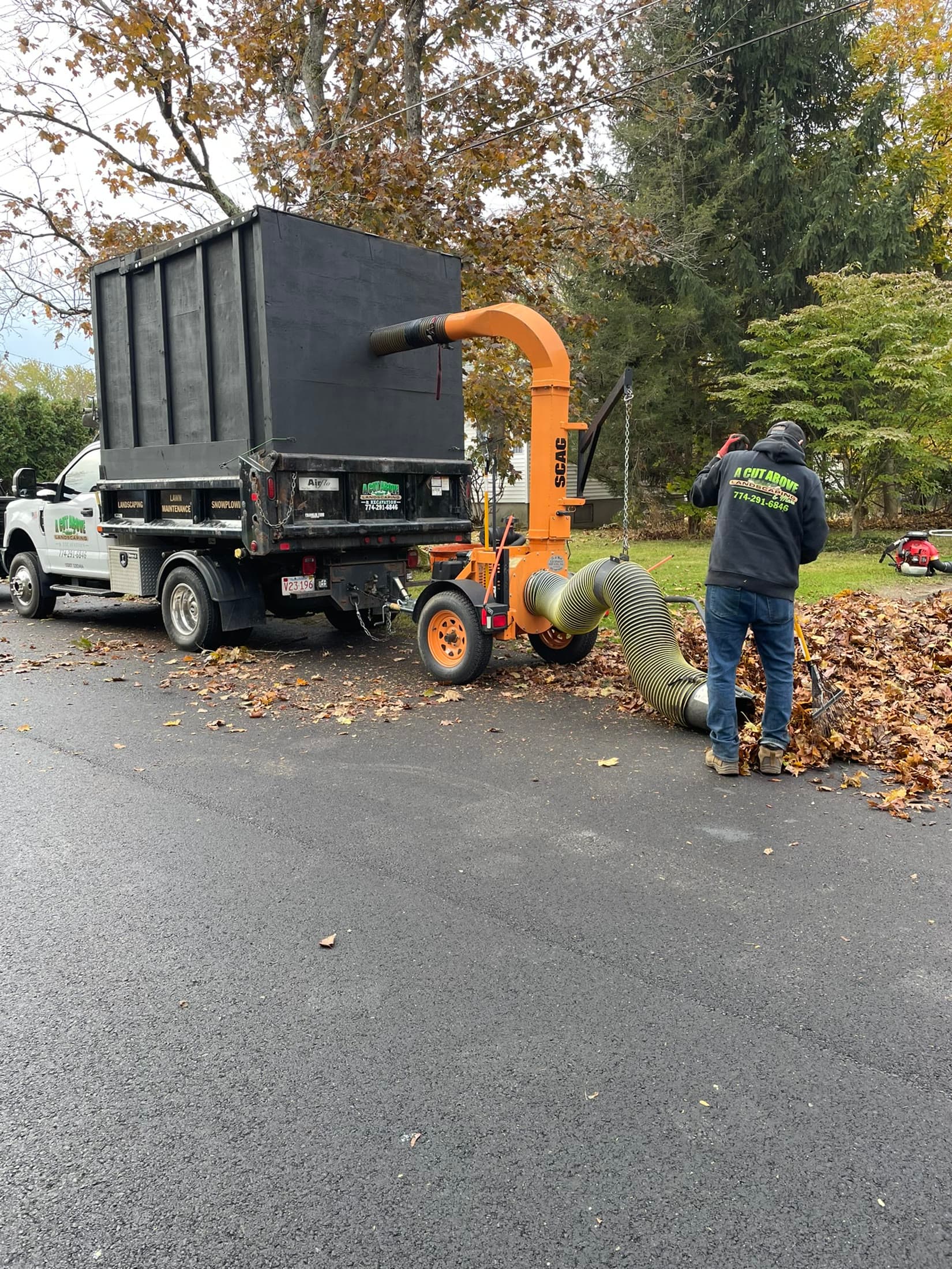 A Cut Above crew collecting autumn leaves with a leaf vacuum and cleanup truck